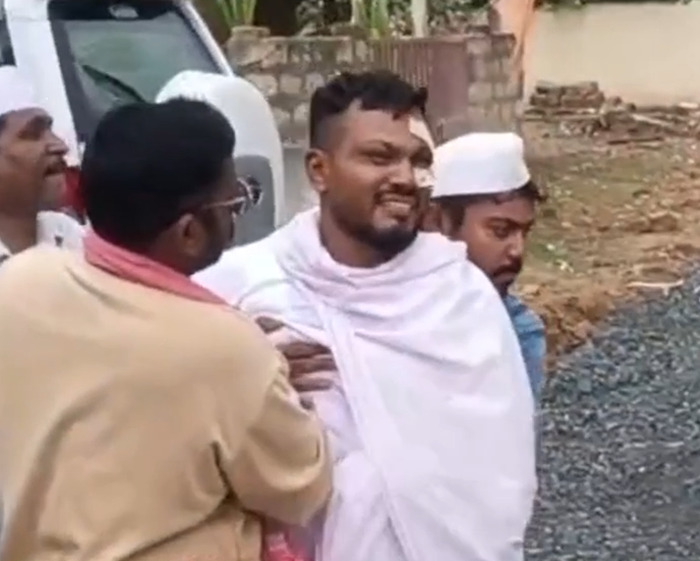 Sole survivor of Air India crash wrapped in white shawl supported by men during emotional moment outdoors.