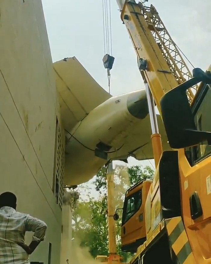 Crane removing damaged plane tail section during Air India crash site clearance with a man watching nearby.