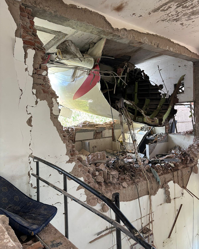 Wreckage of Air India crash visible through broken wall of a building, showing destroyed interior and debris.