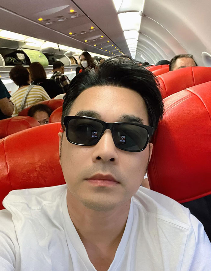 Thai actor wearing sunglasses and white shirt, seated on a plane, linked to Air India&rsquo;s only plane crash survivor story.