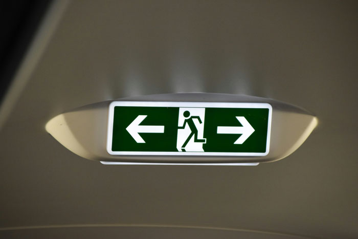 Emergency exit sign on airplane ceiling with arrows pointing left and right symbolizing plane crash survival routes.