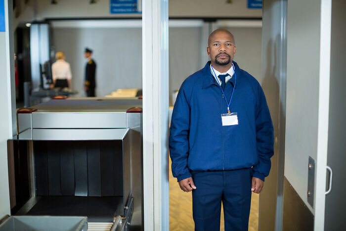 TSA agent standing by security checkpoint to help travelers avoid being held up in security line before boarding.