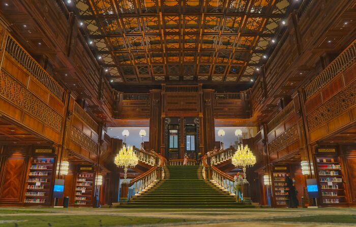 Grand staircase inside a stunning and impressive bookstore with wooden details and elegant chandeliers.