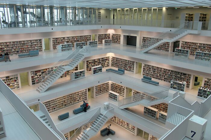 Modern grandiose library interior with multiple floors, white staircases, and extensive bookshelves filled with books worldwide.