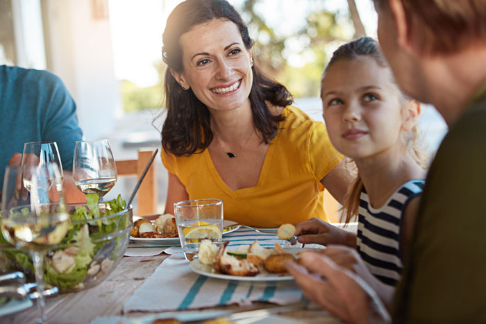 Woman in yellow top smiling at family dinner while discussing solo traveler expected to stop drinking alcohol.