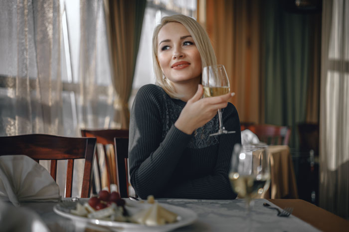 Solo female traveler enjoying a glass of white wine at a restaurant, highlighting women drinking while traveling.
