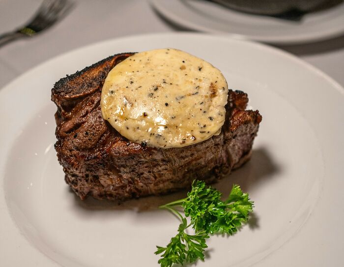 Grilled steak topped with herb butter served on a white plate with a parsley garnish, illustrating American food culture.