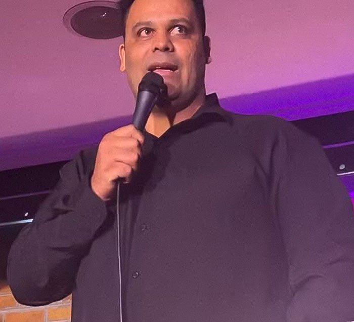 Man in black shirt holding a microphone speaking in front of purple lights related to beauty queen strangled family friend topic