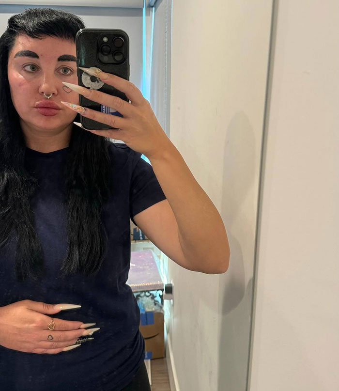 Amanda Bynes taking a mirror selfie indoors, showing long nails and wearing a navy blue shirt after revealing Ozempic use.