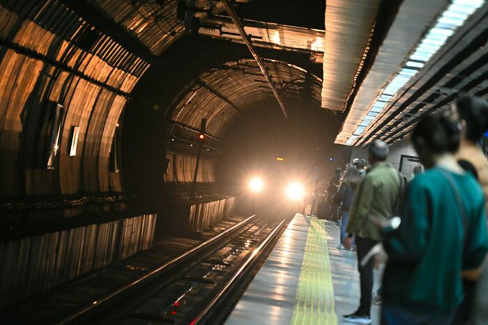Commuters waiting in a subway station as a train approaches, illustrating people still falling for fictional things.