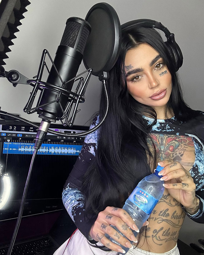 Female singer with tattoos wearing headphones in a recording studio, highlighting plastic surgery tragedy keywords.
