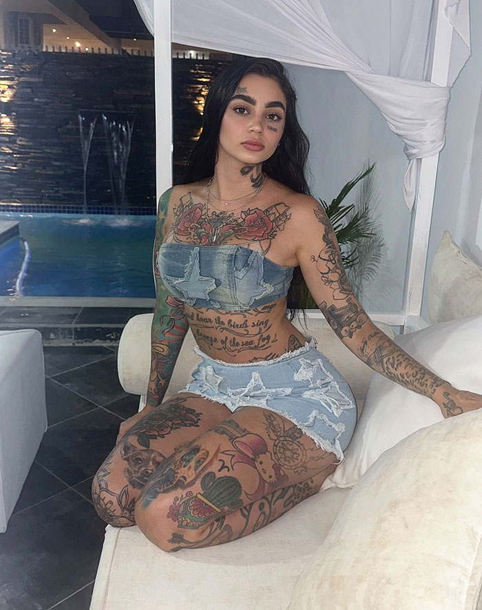Young tattooed woman sitting on a couch by the pool, showcasing bold style and edgy plastic surgery transformation.