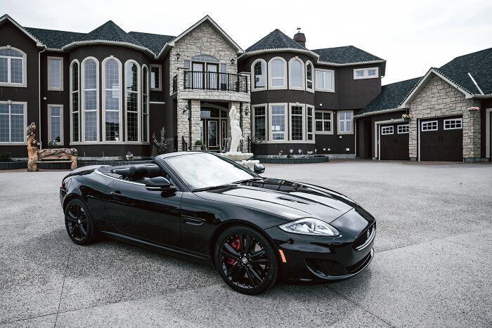 Luxury black convertible parked in front of an expensive mansion.