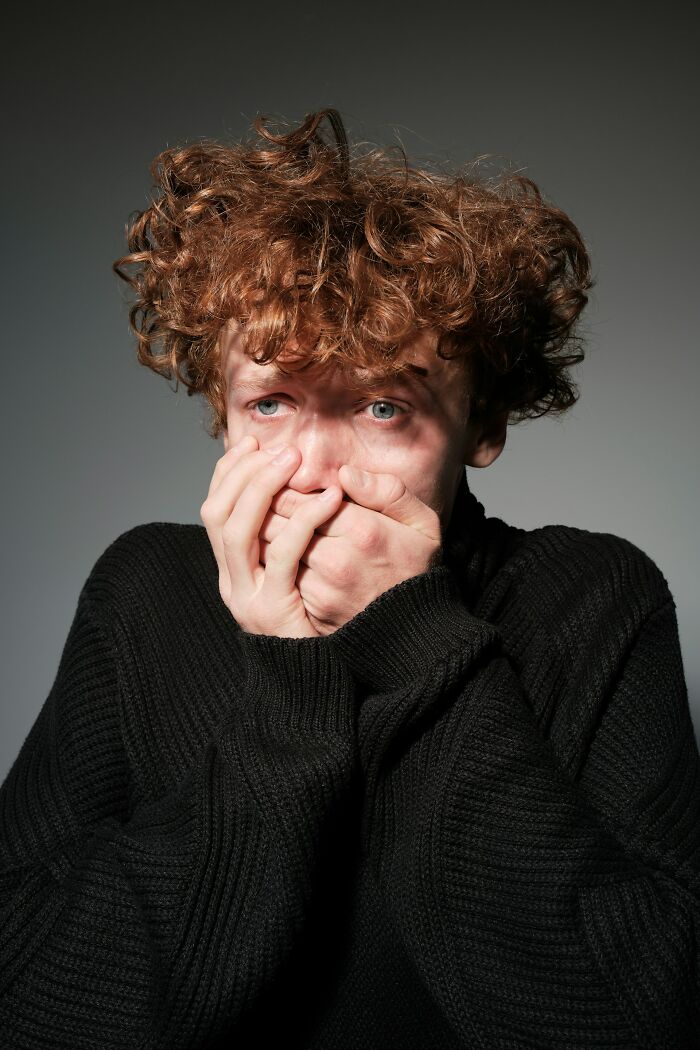 Young man with curly hair covering his mouth, showing fear and anxiety reflecting insane hospital experiences in medical settings.