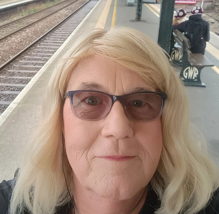 Close-up of a trans woman with glasses at a train station, related to trans woman swims topless competition protest.