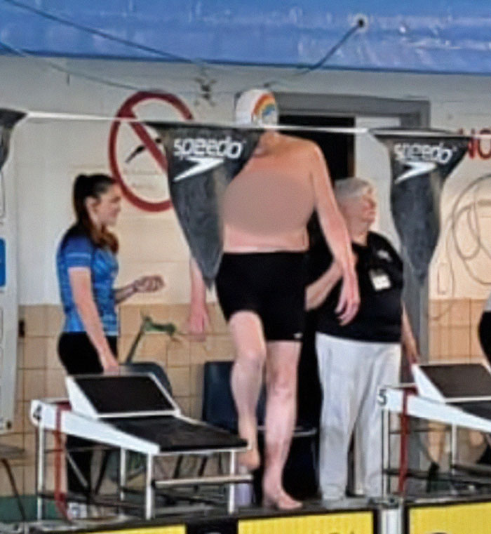 Trans woman swims topless during swim competition against men wearing black shorts and rainbow swim cap.