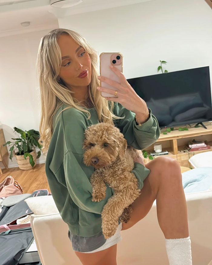 Young woman taking selfie holding dog in living room, related to woman who slept with 583 men and assault by co-star.