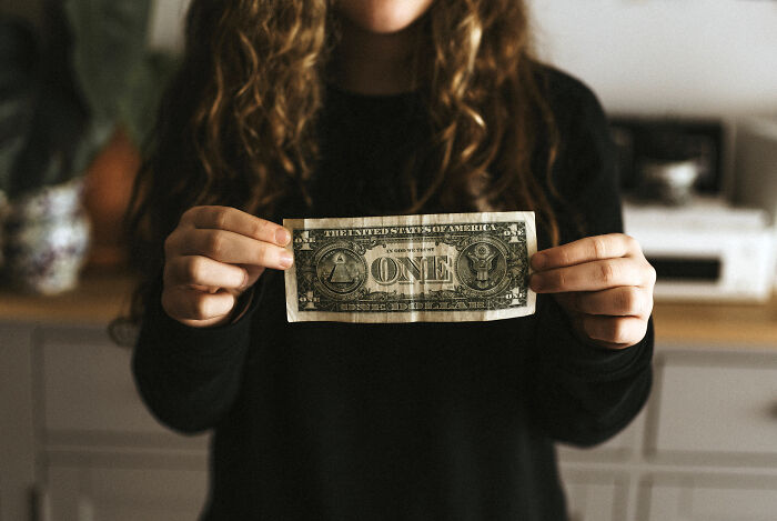 Person holding a one dollar bill, illustrating tales of a priceless reward after spending just a dollar.