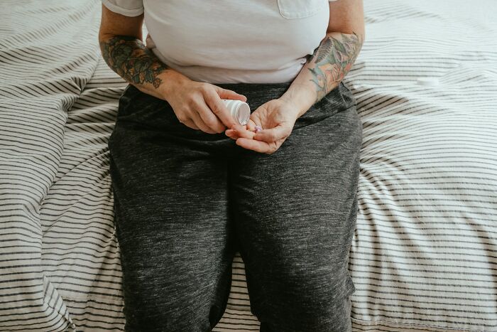 Person with tattoos sitting on a bed holding pills from a bottle, an everyday item under $300 improving lives.