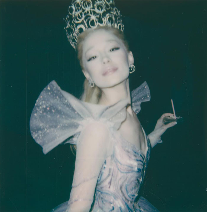 Ariana Grande wearing a sparkling costume with an ornate headpiece in a dark setting, highlighting her entirely visible ribcage look.