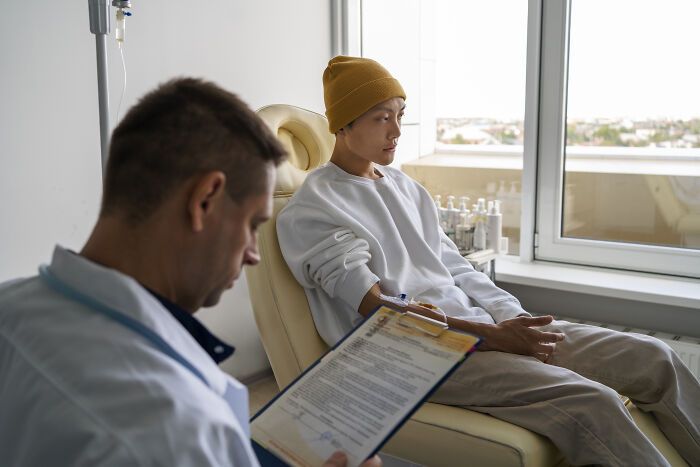 Patient wearing a yellow beanie receiving treatment while doctor reviews notes, highlighting tobacco risks in oncology care.