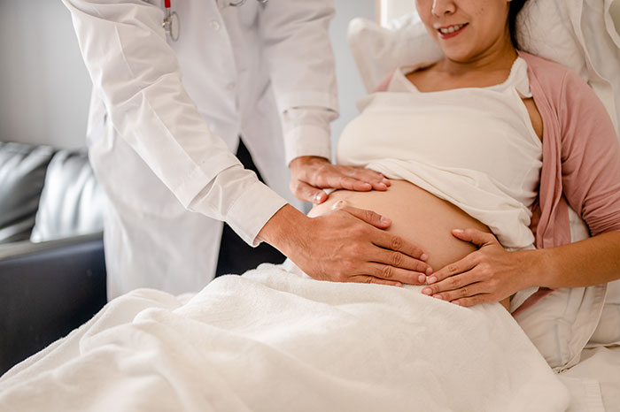 Doctor examining pregnant woman in delivery room, highlighting man furious after wife removes him over prank.