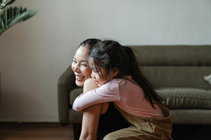 Young mom smiling and hugging her child in a living room, illustrating family dynamics and legacy challenges. Young mom smiling and hugging her child in a living room, illustrating family dynamics and legacy challenges.