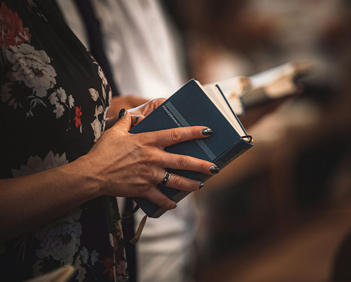 Christian woman holding a book in a floral dress, symbolizing faith and therapy skepticism in a quiet indoor setting.