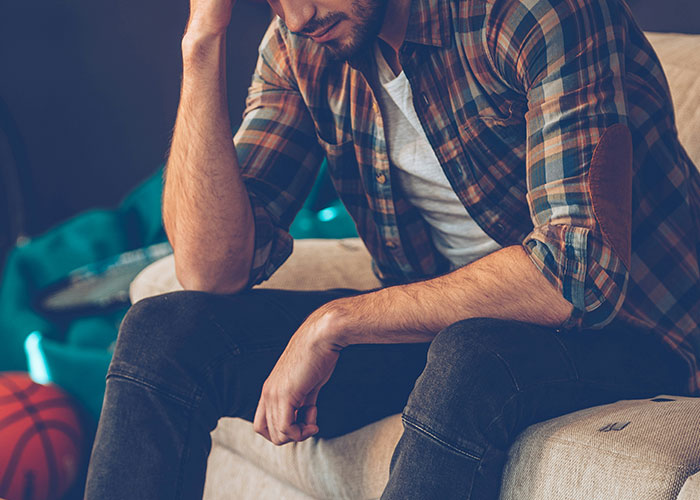 Man in plaid shirt sitting on couch, appearing deep in thought, illustrating strange things autopsy doctors discover.