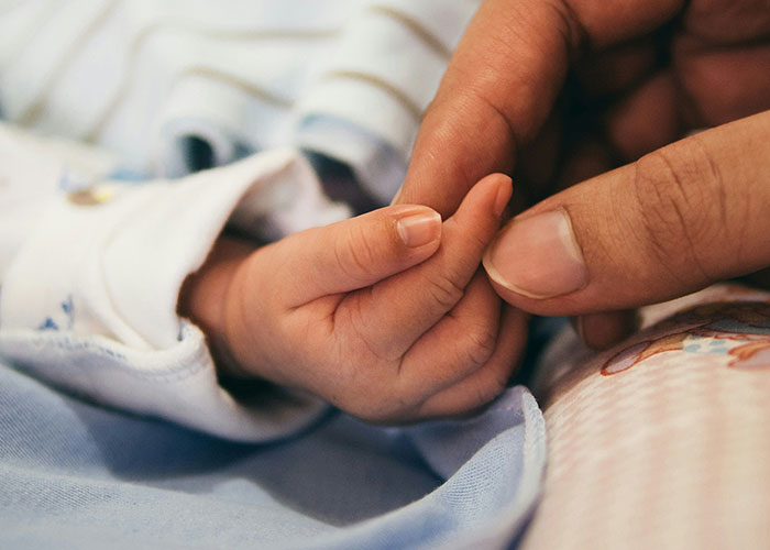 Close-up of a baby’s hand gently holding an adult finger, illustrating human connection in autopsy doctors’ strange discoveries.