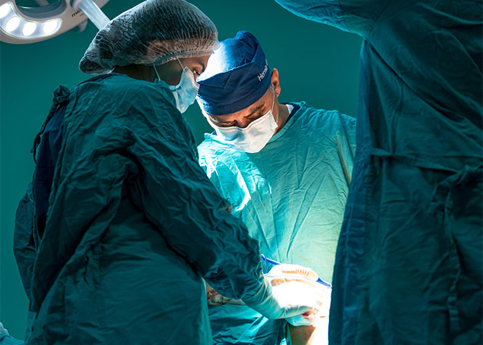 Autopsy doctors in surgical gowns and masks performing a detailed examination under bright operating room lights.