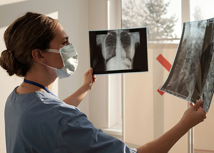 Female autopsy doctor wearing mask examining X-rays in a bright room, highlighting strange autopsy discoveries on the job.