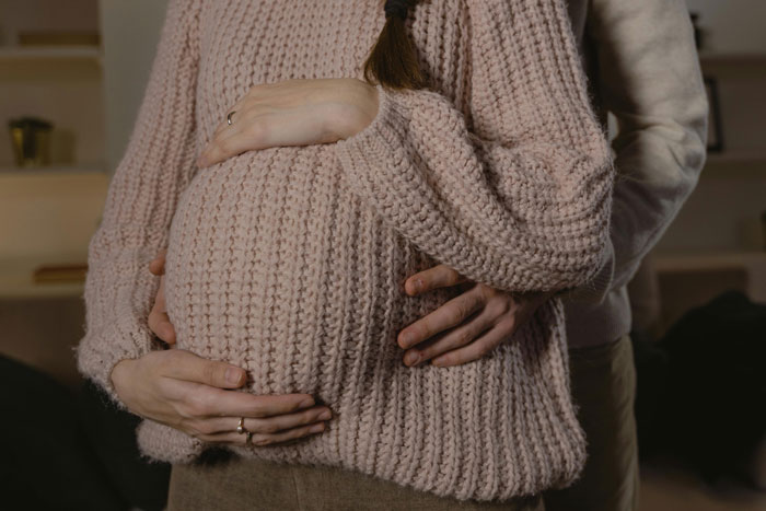 Pregnant woman wearing pink sweater with hands on belly, illustrating MIL convinced baby gender was manipulated conflict.