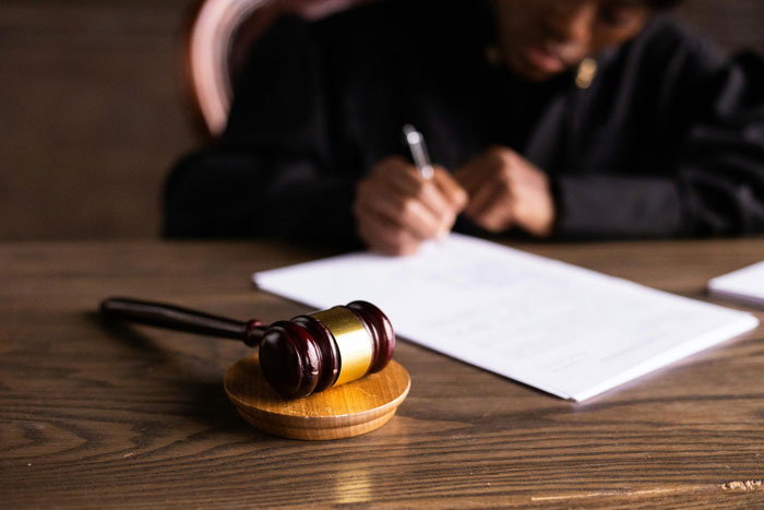 Close-up of a wooden gavel with a person writing legal documents in the background about MIL, pregnant DIL, and divorce.