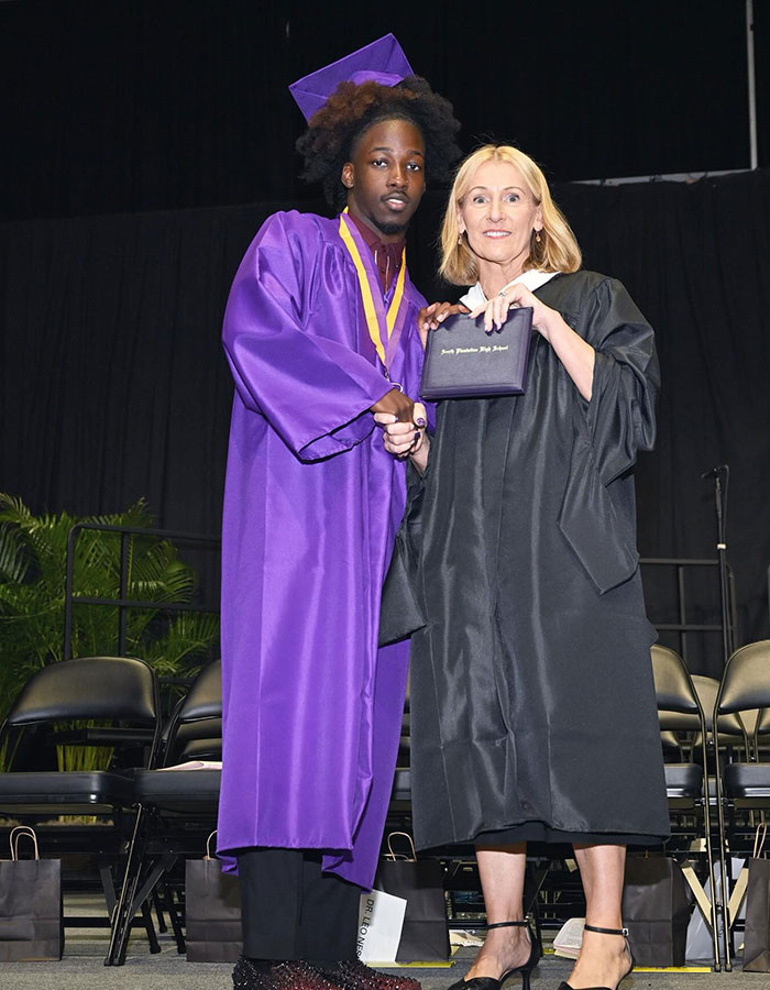 Florida high school grad in purple cap and gown shakes hands with faculty during graduation ceremony stage mishap event.