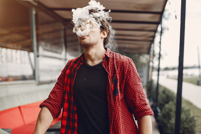 Young man wearing a red plaid shirt exhaling a cloud of smoke, illustrating bad things people face in life.