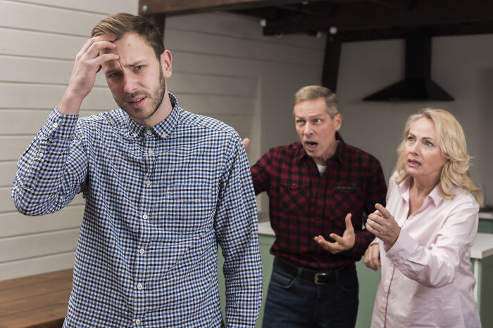Young man looking stressed while an older couple argues angrily behind him, illustrating bad things in people’s life.