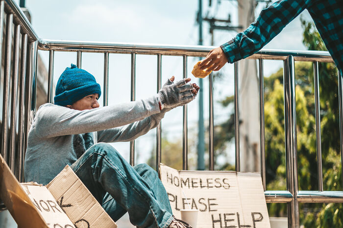 A person giving food to a homeless man sitting outdoors, highlighting bad things people face in life.