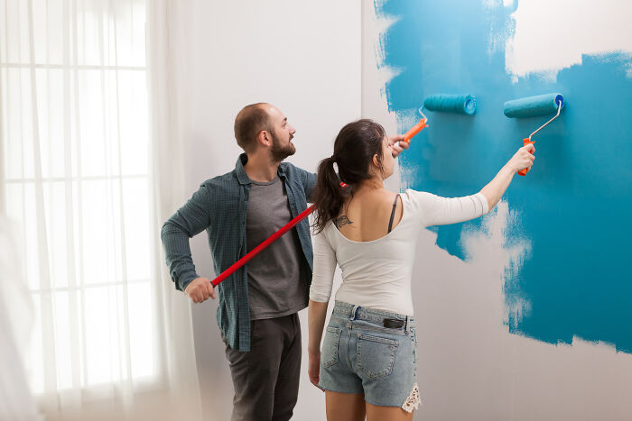 Couple painting a wall blue together, illustrating bad things people face in life through teamwork and change.