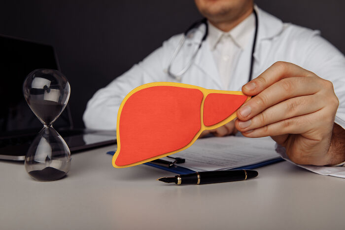 Doctor holding a paper liver model near an hourglass, illustrating bad things people face in life related to health.