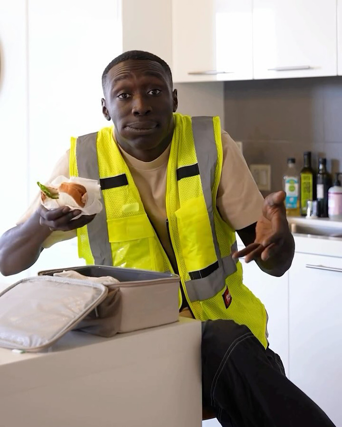 Young man in a yellow safety vest eating a sandwich indoors, related to Barron Trump friend and Khaby Lame ICE detention claims. Young man in a yellow safety vest eating a sandwich indoors, related to Barron Trump friend and Khaby Lame ICE detention claims.