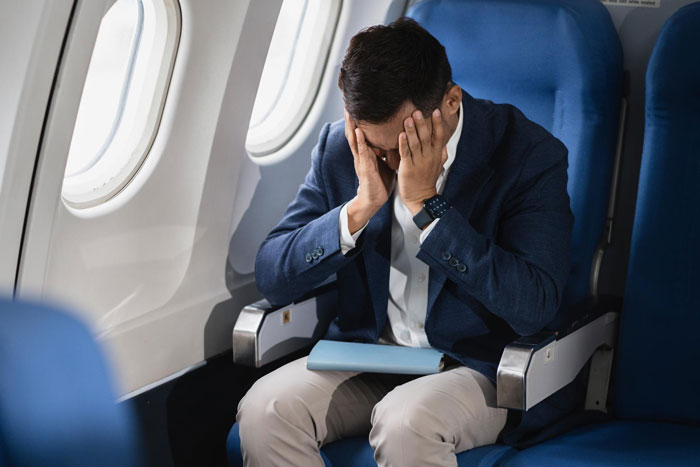 Man mid-flight meltdown covering face in airplane seat, illustrating parenting versus passenger debate over screaming baby.