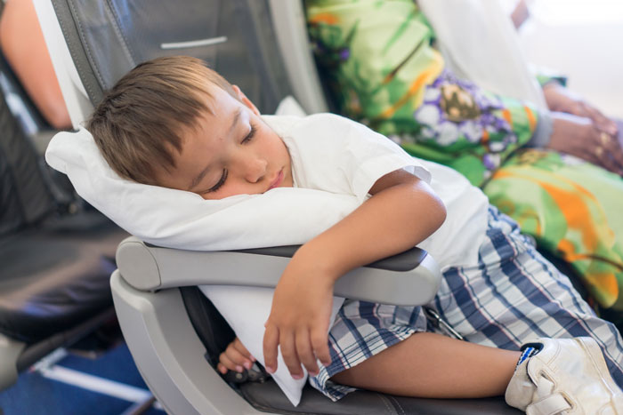 Young boy sleeping on an airplane seat using a pillow during a mid-flight scene related to parenting versus passenger debate.