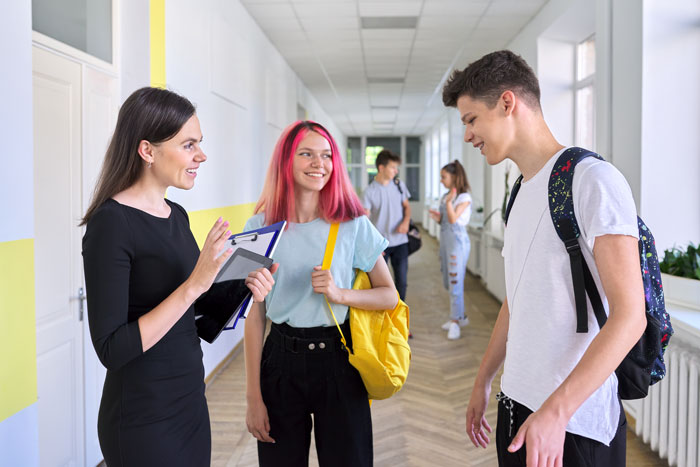 High school students talking with a teacher in hallway, highlighting educators' concerns about county knowledge gaps. High school students talking with a teacher in hallway, highlighting educators' concerns about county knowledge gaps.