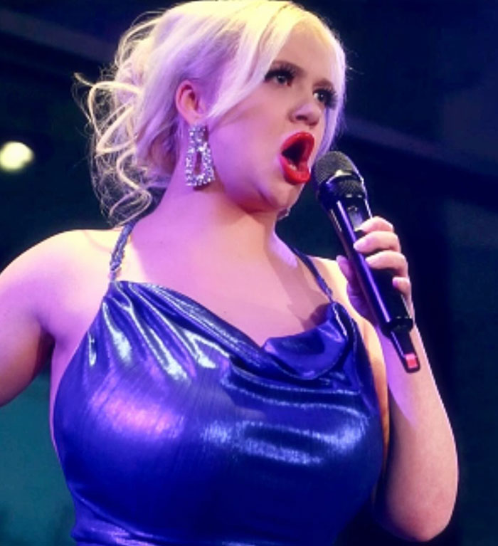 Singer and Greta Thunberg's sister performing on stage, wearing a shiny blue dress and holding a microphone.