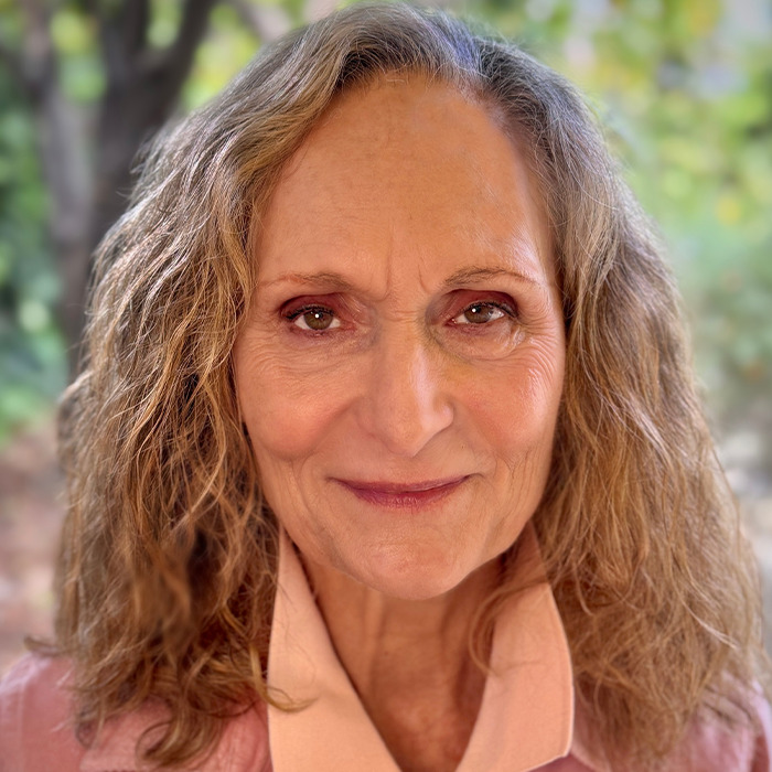 Older woman, beloved 90s star and Rain Man co-star, smiling outdoors with natural curly hair and soft lighting.