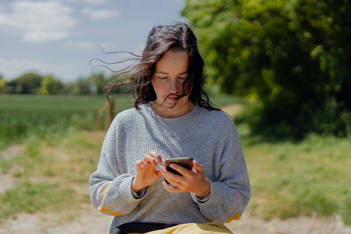 Young woman outdoors using smartphone, reflecting on unhinged ways people got back at their cheating exes.