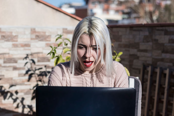 Woman with blonde hair shocked while looking at laptop screen outdoors, symbolizing best friend drama and secret babies.
