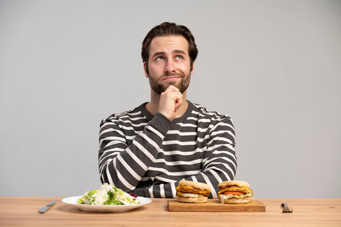 Man in a striped shirt deciding between best processed foods and a healthy salad for weight loss at a wooden table