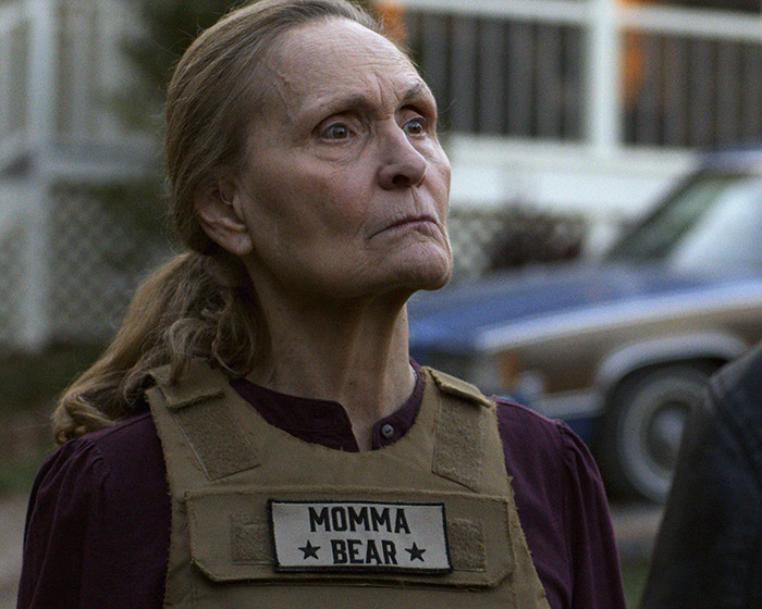 Elderly woman wearing a Momma Bear vest, portraying a beloved 90s star and Rain Man co-star unrecognizable 37 years later.